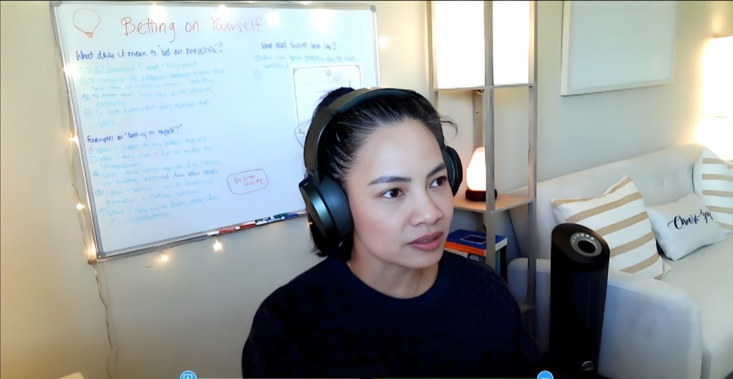 Anne Espiritu on a video call, wearing headphones, with a whiteboard of handwritten notes behind her.